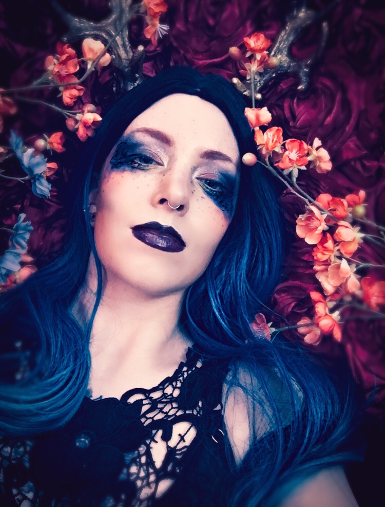 Floral glamour portrait of a genderqueer model with blue hair on a bed of flowers
