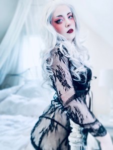 Photography of a feminine character sitting on a beautiful canopy bed lit with natural window light. Sensual portrait photo with rich housewife vibes. Featuring long whit hair and black lace fashion 