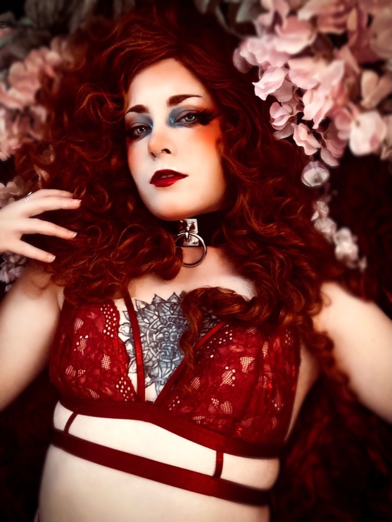 Boudoir self portrait photograph featuring curly red hair, red lace lingerie, and a backdrop of flowers. 
Photographed in the Blessed Shadows photography studio